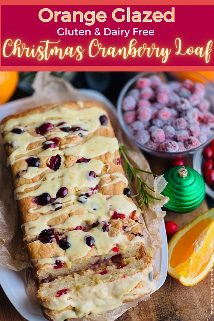 A white bread dish with a cream colored rectangle loaf that has been cut into slices with red circle cranberries popping out of the bread. A light orange colored glaze is drizzled over the top.
