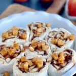 a white pie plate with 7 round dough ball cinnamon rolls with apple chunks on top.