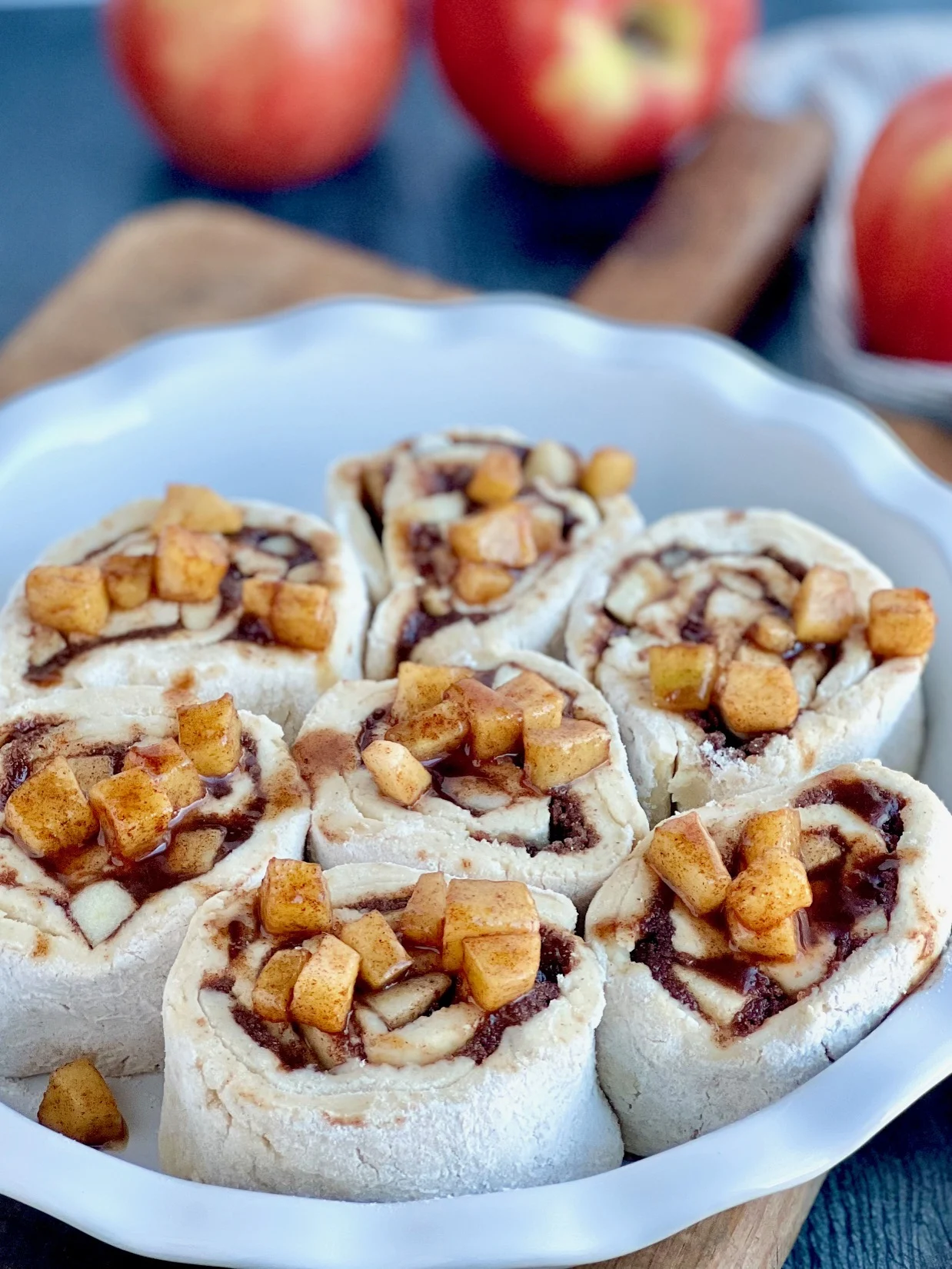 a white pie plate with 7 round dough ball cinnamon rolls with apple chunks on top.