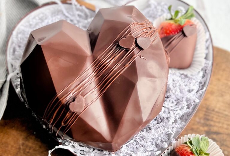 A hollow chocolate heart filled with treats. The outside of the heart has melted chocolate drizzled across it and mini chocolate hearts.