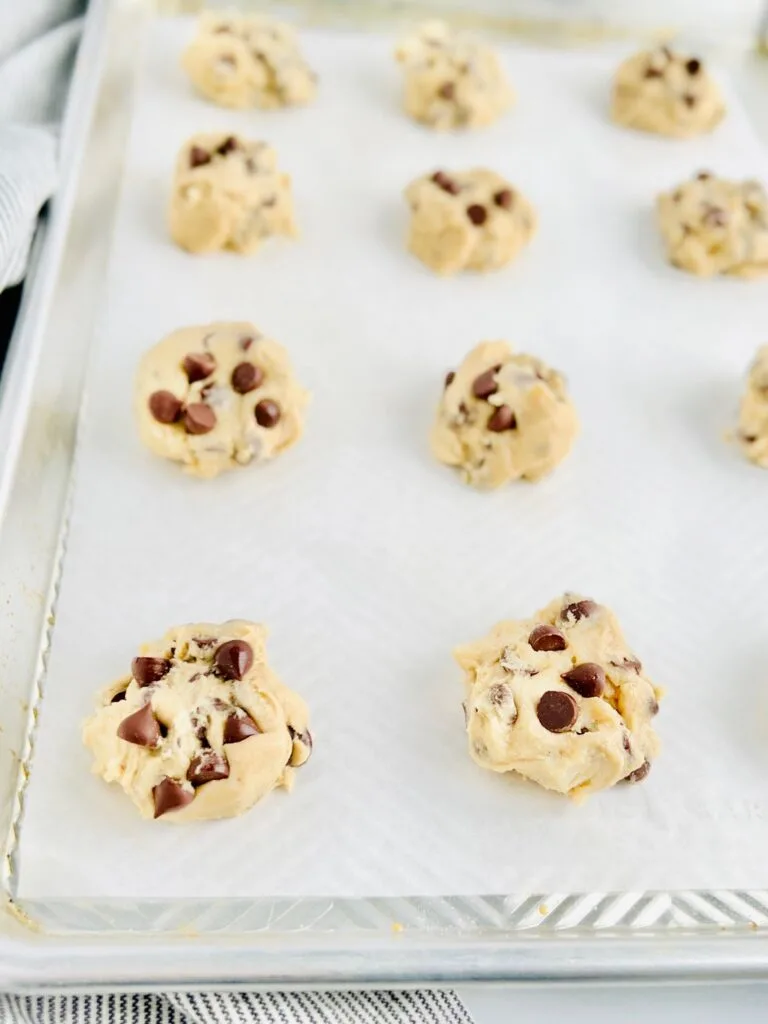 A large cookie baking sheet with raw cookie dough balls on it before it goes into the oven.