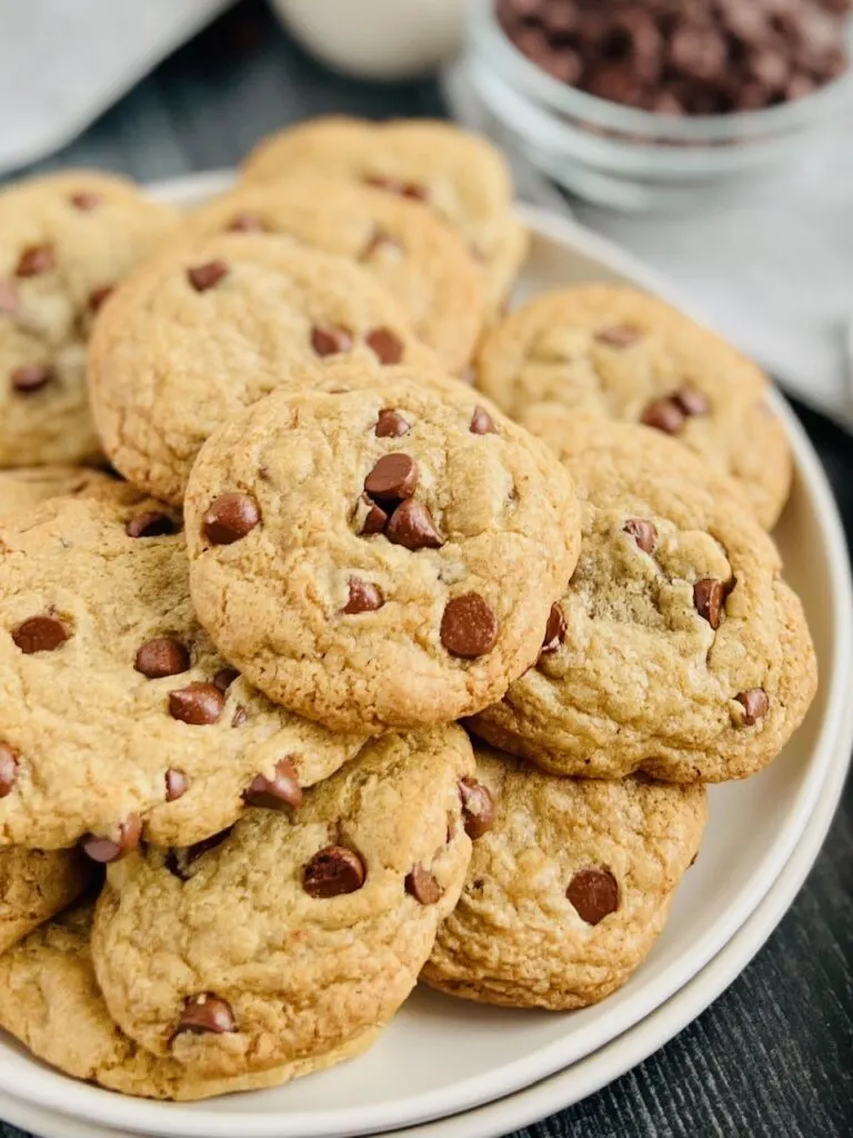 A large white plate with layers of small, round chocolate chip cookies on it.
