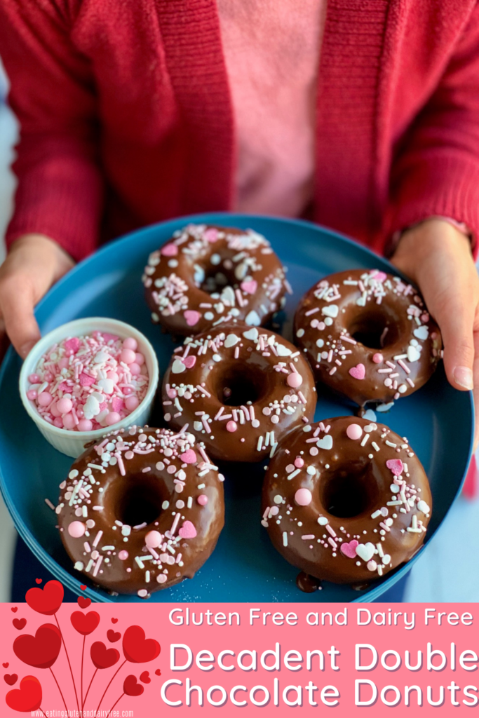 A blue plate full of chocolate donuts with white and pink sprinkles on them.