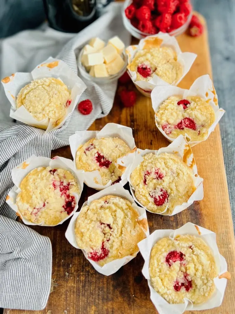 8 light colored muffins with speckles of red raspberries popping through on a wood cutting board.