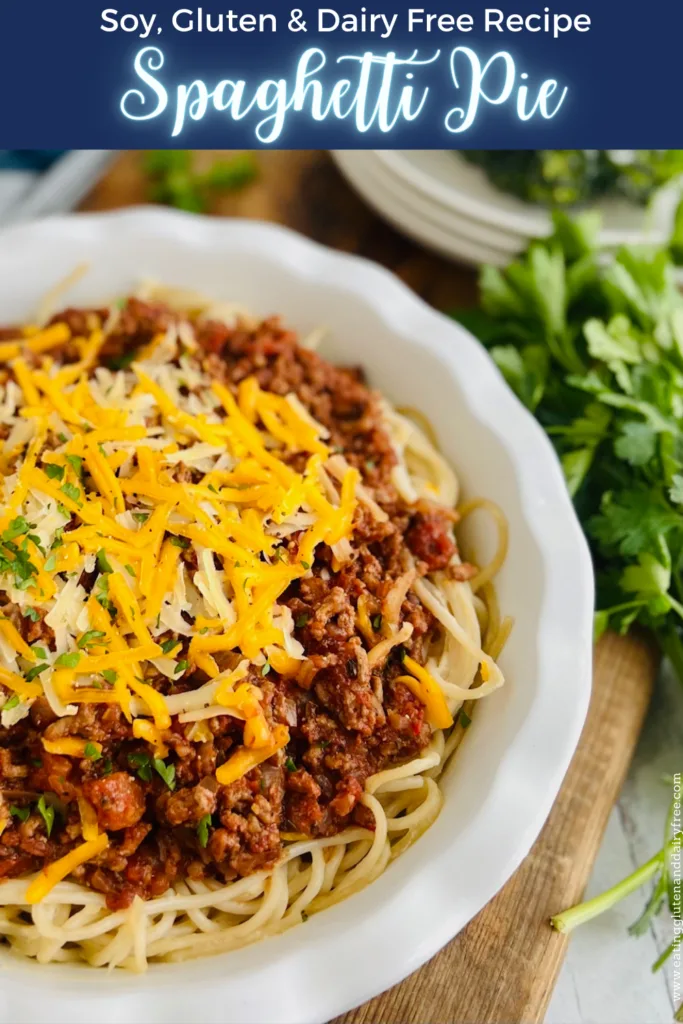 A white pie dish layered with long spaghetti noodle's on the bottom, then a red pasta meat sauce and topped with chopped up parsley and grated yellow cheese on a wood cutting board.