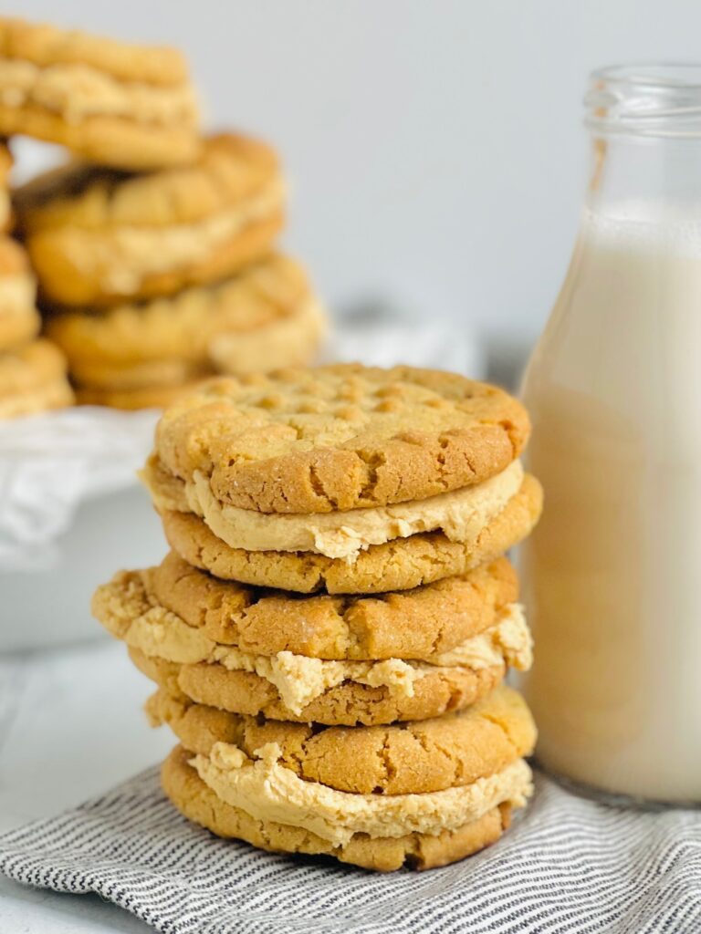 A stack of 3 peanut butter cookies with a brown peanut butter frosting in the middle next to a bottle of milk.