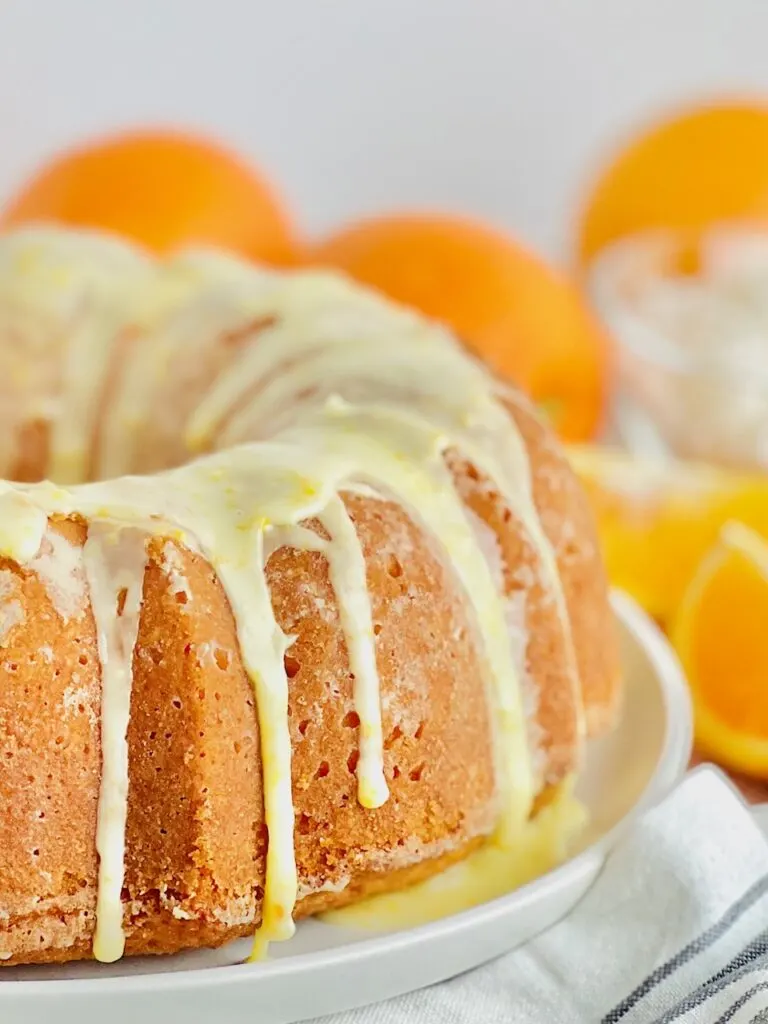 A circle shaped bundt cake with a light colored glaze over the top of the cake on a white serving dish..