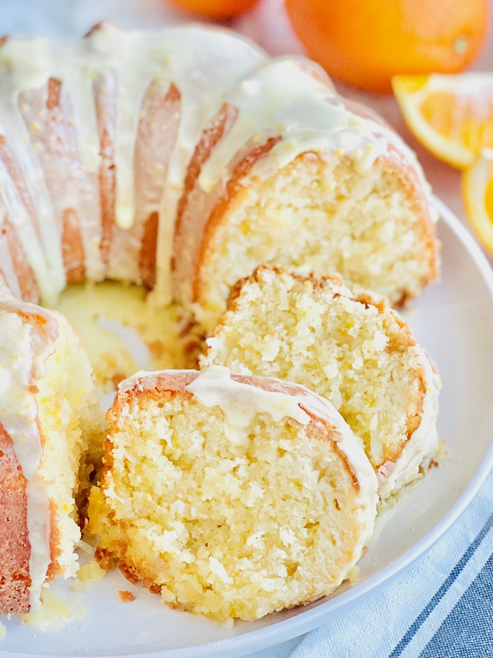 A circle shaped bundt cake with shredded coconut and fresh orange zest cut into slices. There is a light colored glaze over the top of the cake.