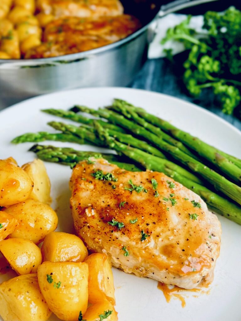 A dinner plate filled will mini golden potatoes, a large piece of light colored meat with a dark red sauce across the top and bit of Italian parsley, and a bunch of sautÃ©ed asparagus. 