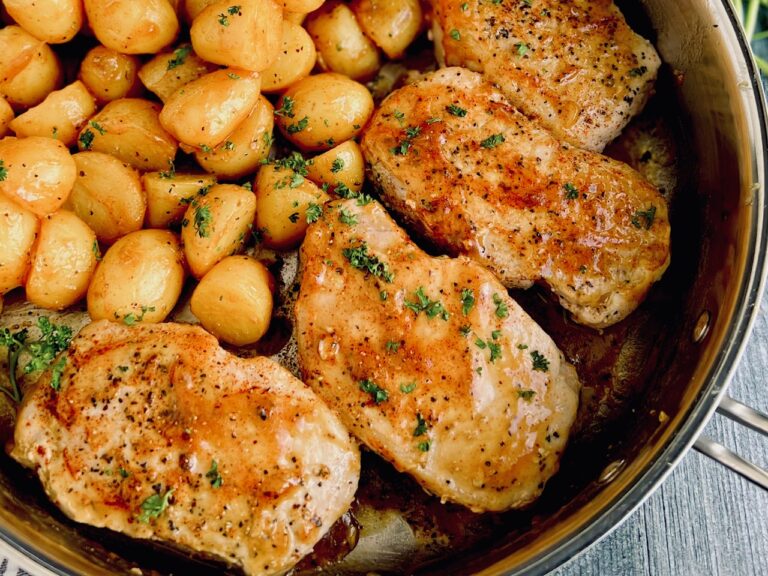 A shiny pan filled with 4 thick light pieces of meat topped with a dark red glaze next to several mini potatoes.