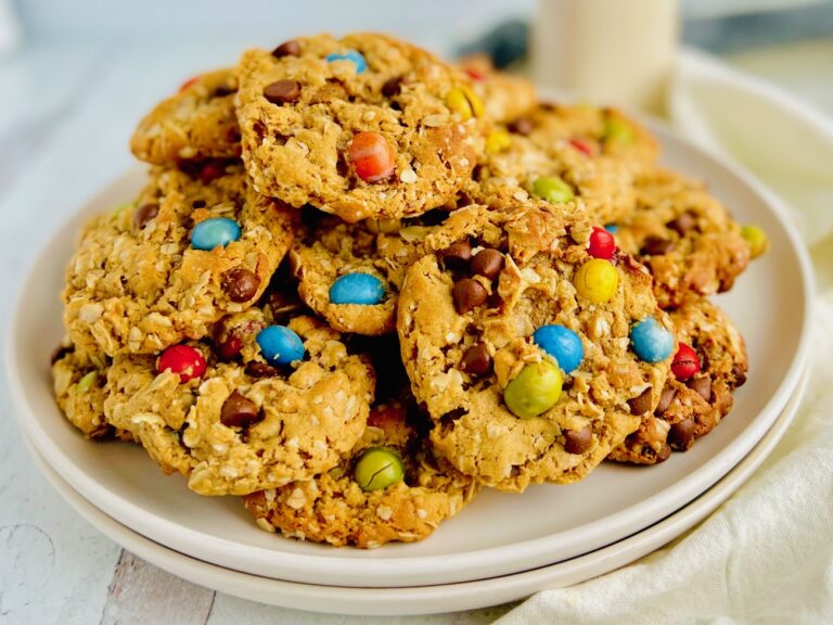 A white plate full of cookies with oats, creamy peanut butter, chocolate morsels, and chocolate candies.