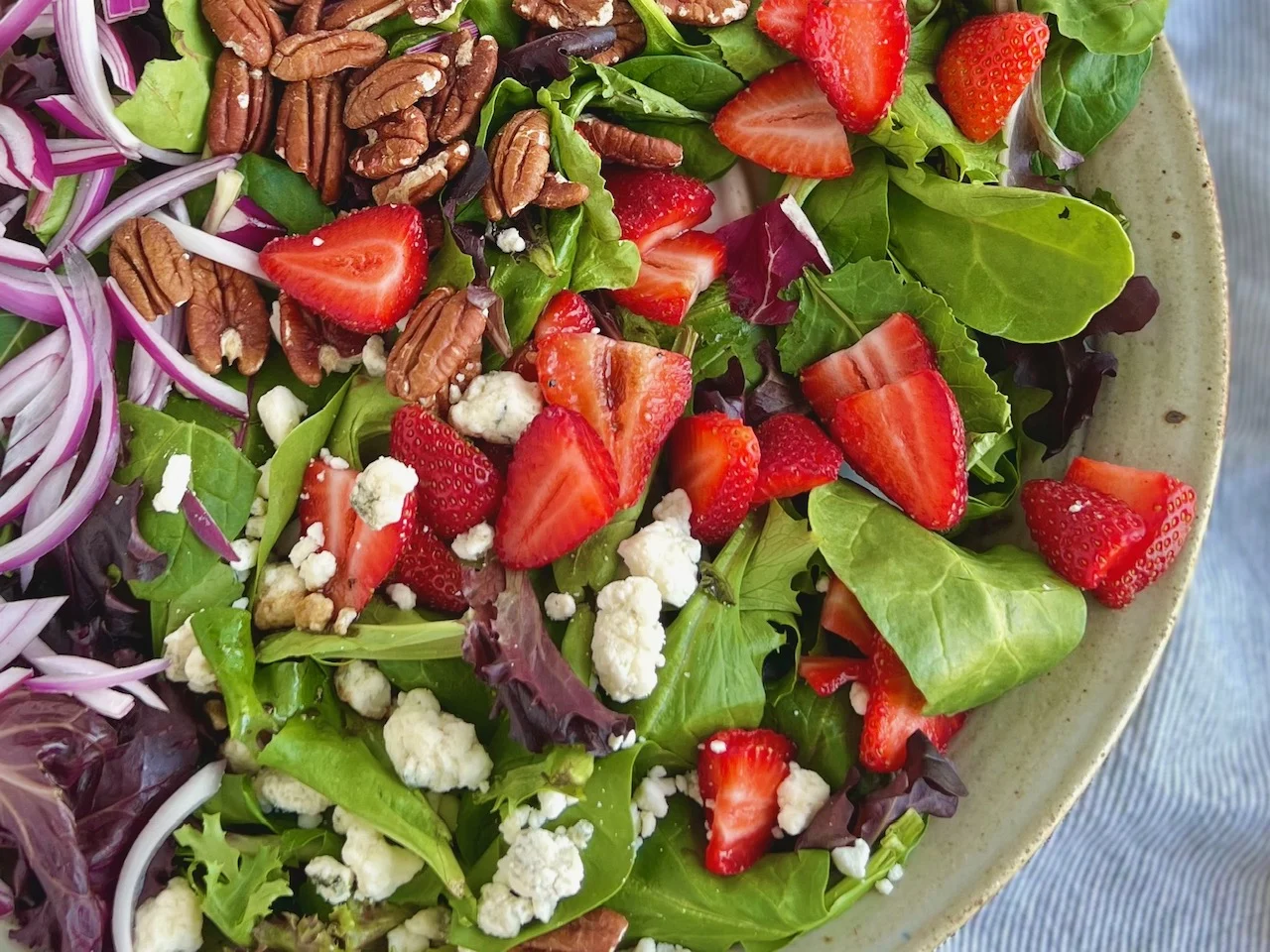 A corner view of a salad bursting with strawberries, white bleu cheese, pecans, and red onion.