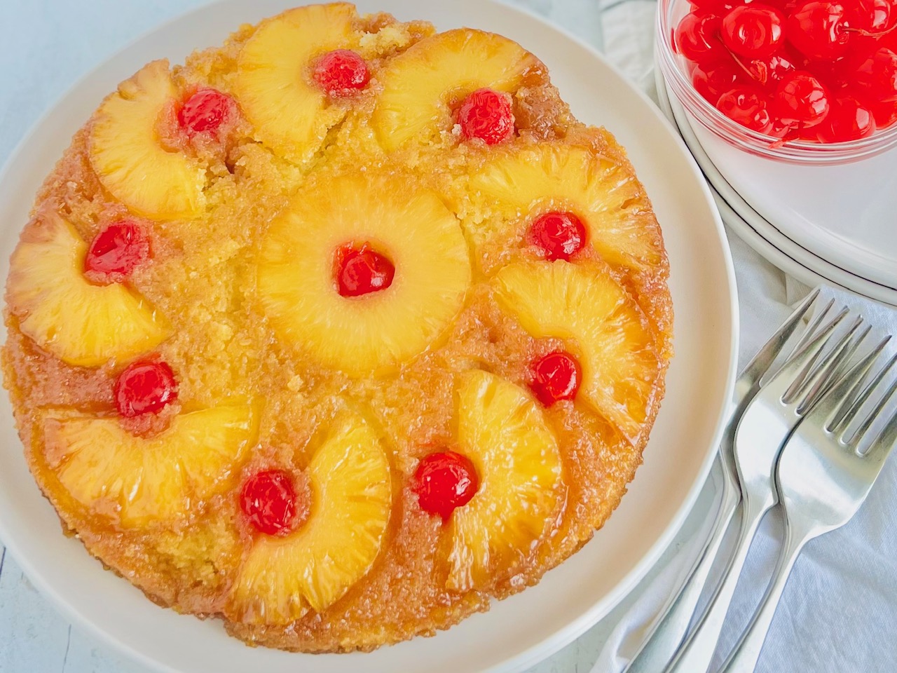 A round yellow brown cake with decorative slices of pineapple slices and red cherries on the top.