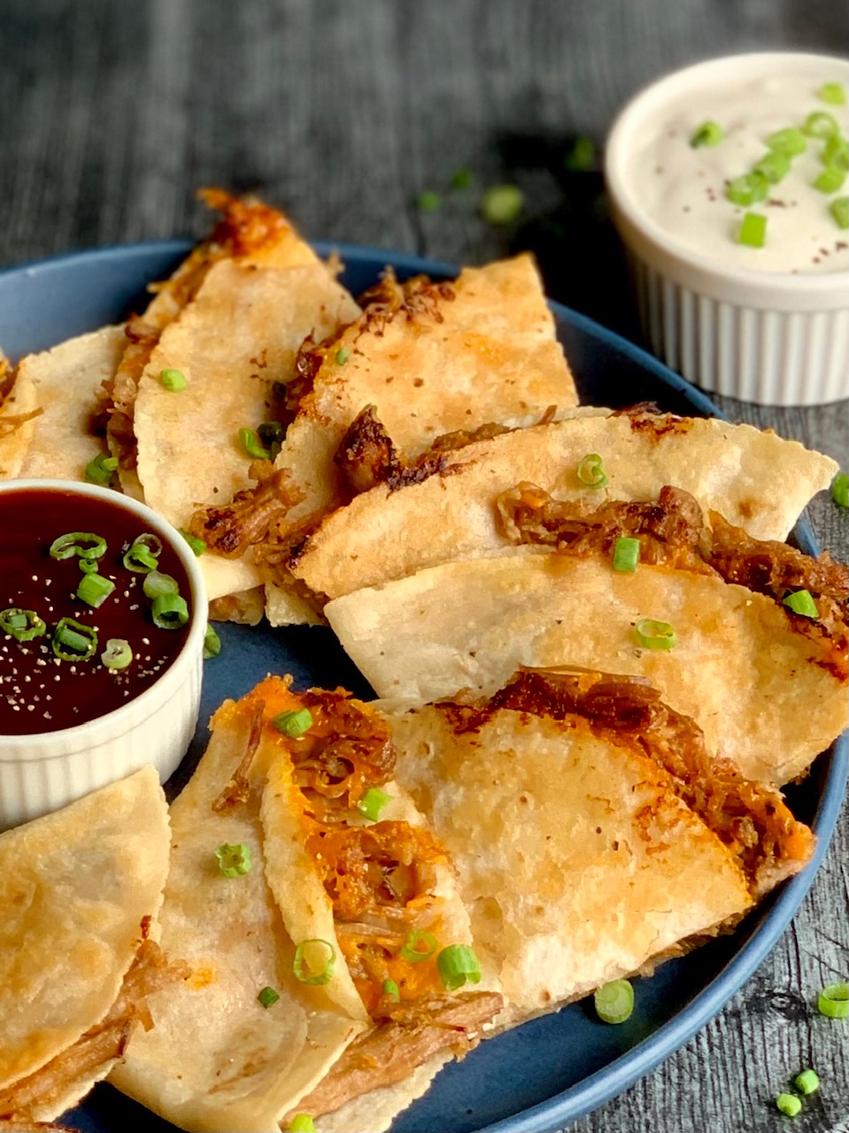 A blue plate will with cut crispy looking tortillas with a brown pulled pork sticking out and yellow melted cheese.