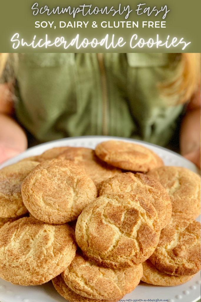 A person with a green jumpsuit holding a white plate of round baked cookies with a crackly cinnamon and sugar topping.