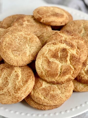 A white plate loaded with round cookies with a crackly brown and white top.