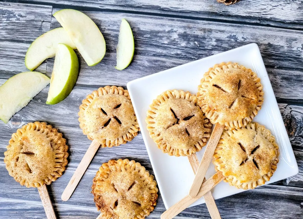 Apple slices next to a plate of pie pops on a plate.
