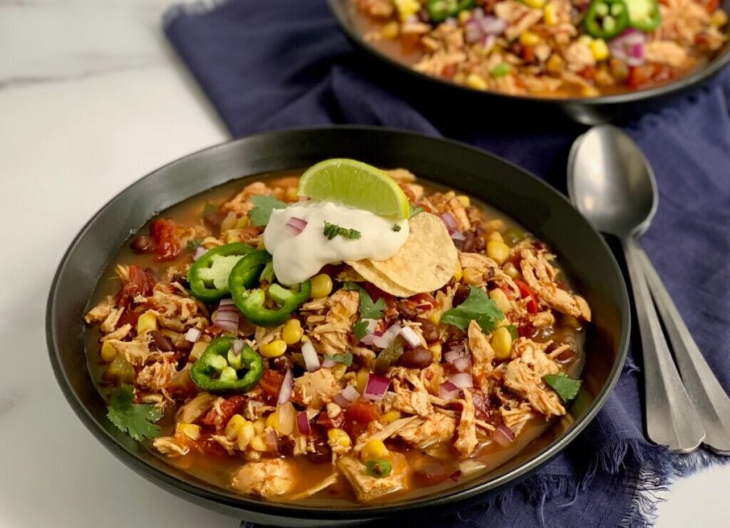 Black bowl of taco soup with spoons next to it.
