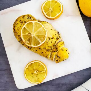 Looking down on chicken breast with lemon on a white plate.