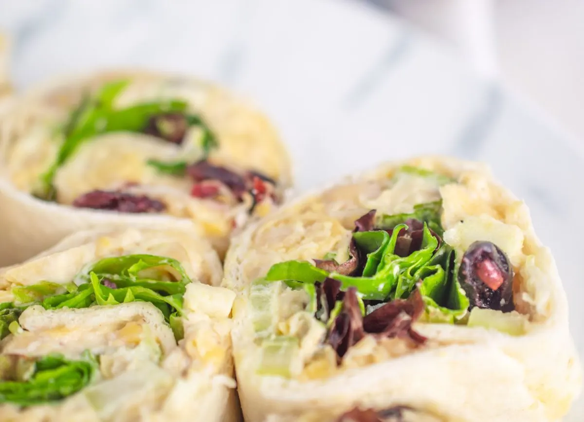 A pinwheel and a tortilla filled with lettuce chickpeas cranberries and apples.