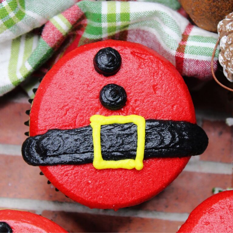 A close-up of a single cupcake that is made with gluten and dairy free ingredients and decorated to look like Santas Billy with his belt and coat buttons.