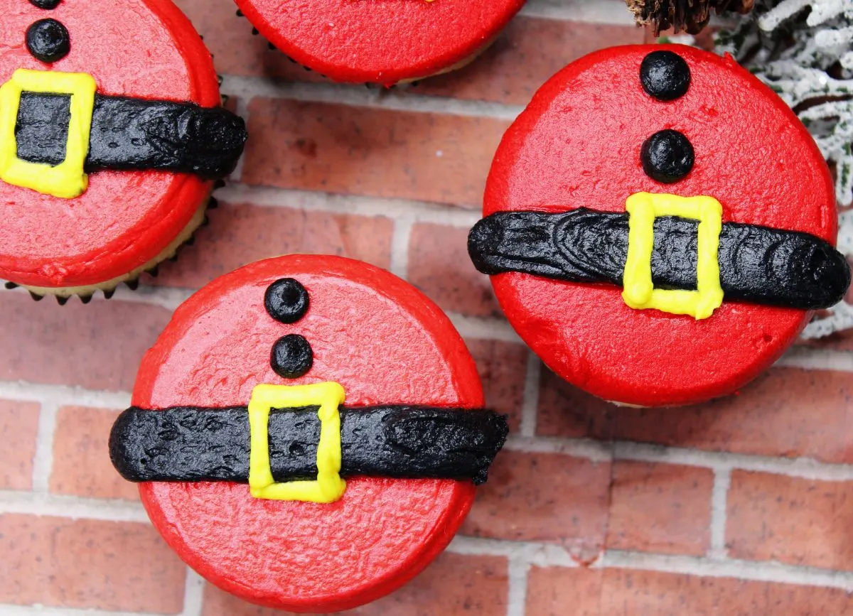 A close-up image of to gluten and dairy free cupcakes decorated to look like Santa belly.