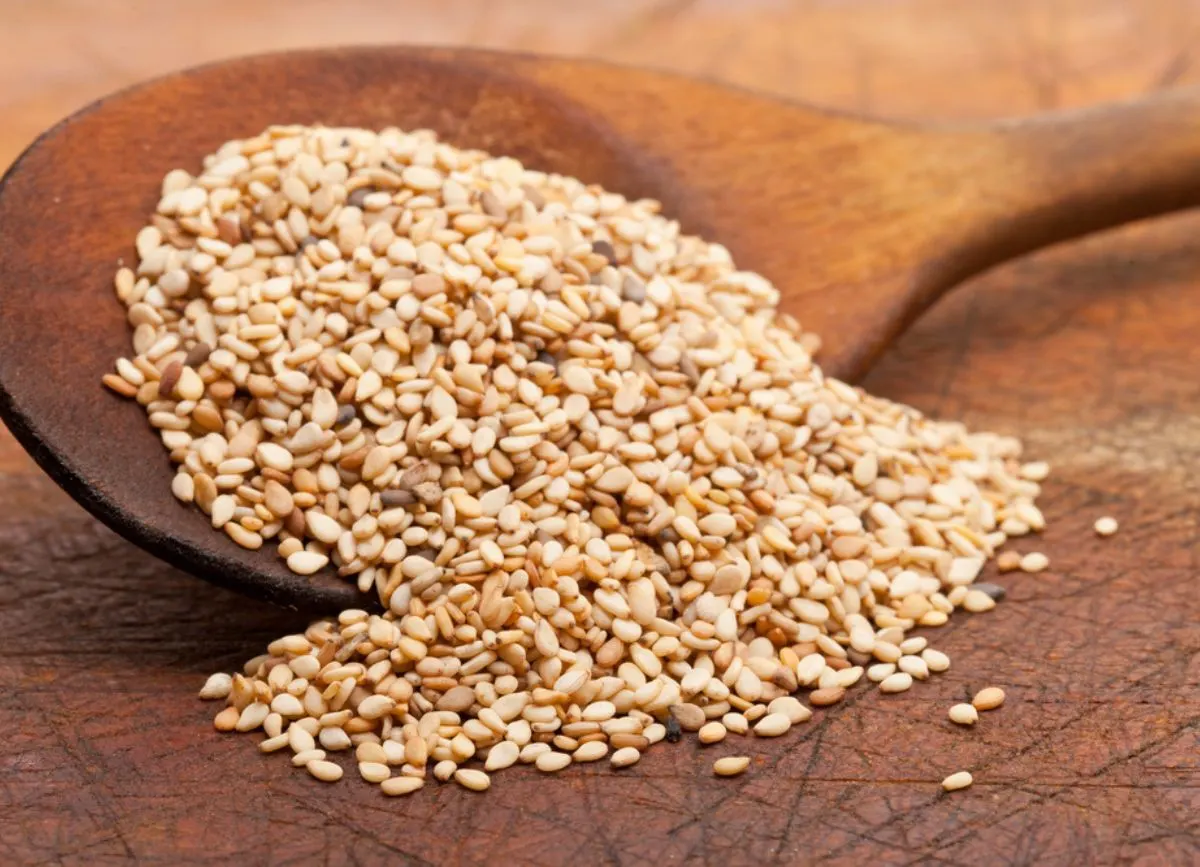 A wooden spoon spilling a pile of sesame seeds.