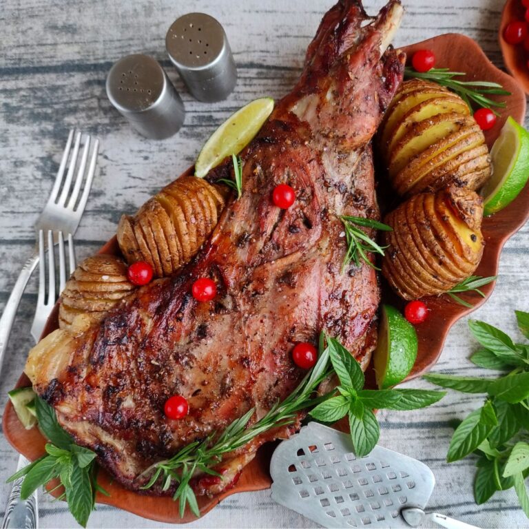 Roasted lamb leg on a platter with garnishes and potatoes.