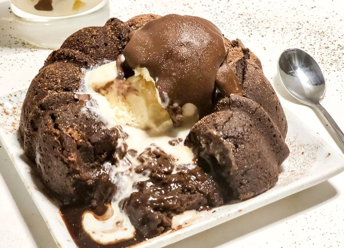 A plate with a chocolate molten lava cake that's been broken into. 