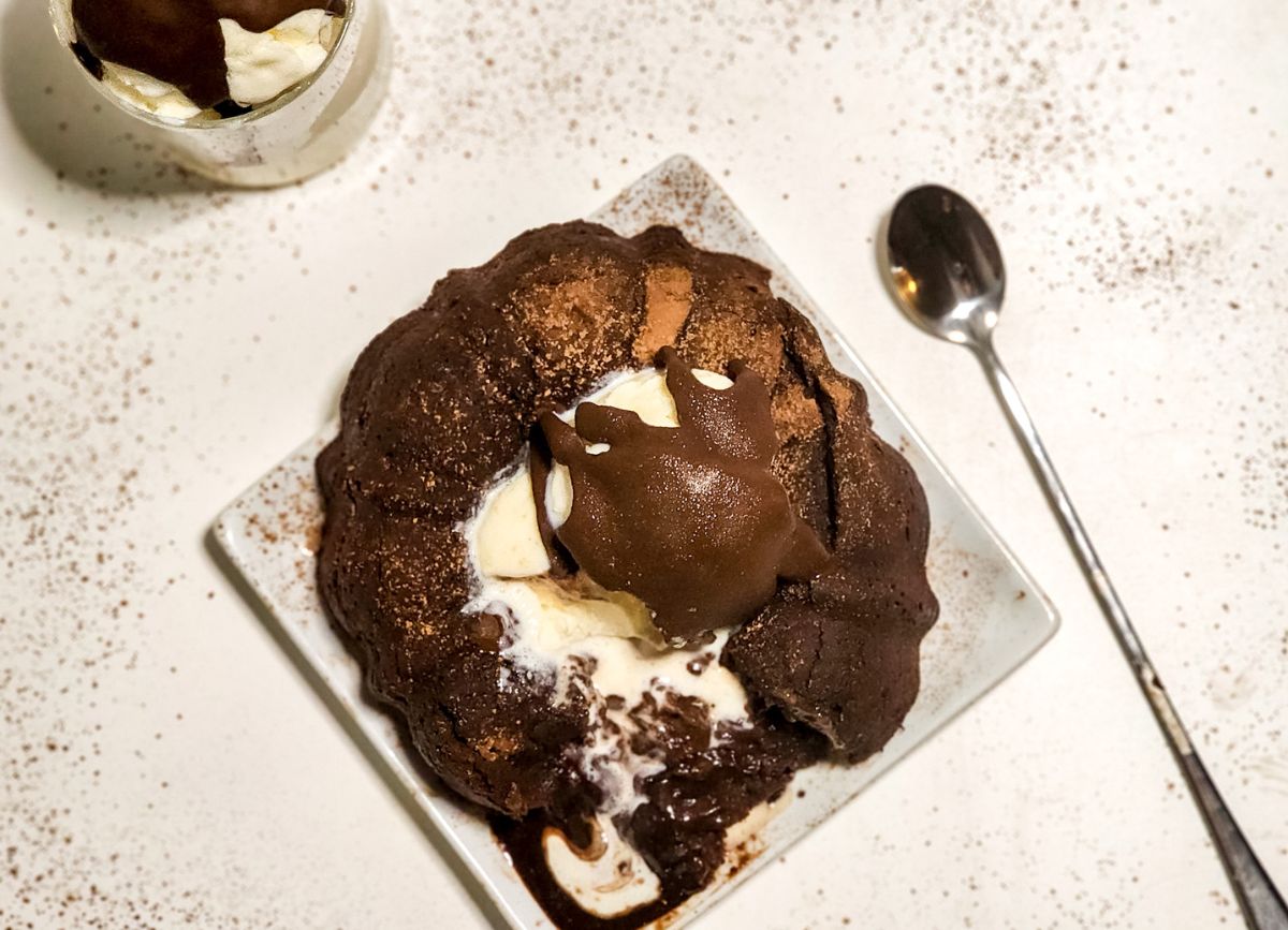 A chocolate molten lava cake broken open on a plate with a spoon next to it.
