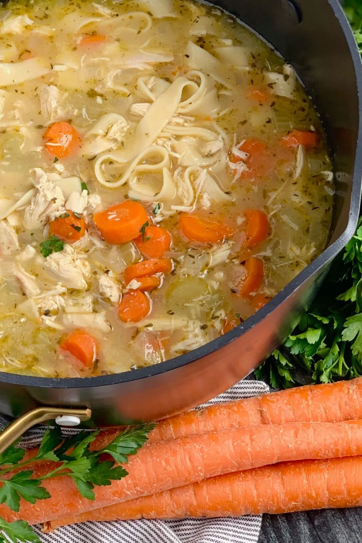 A pot of Chicken Noodle Soup and carrots. 