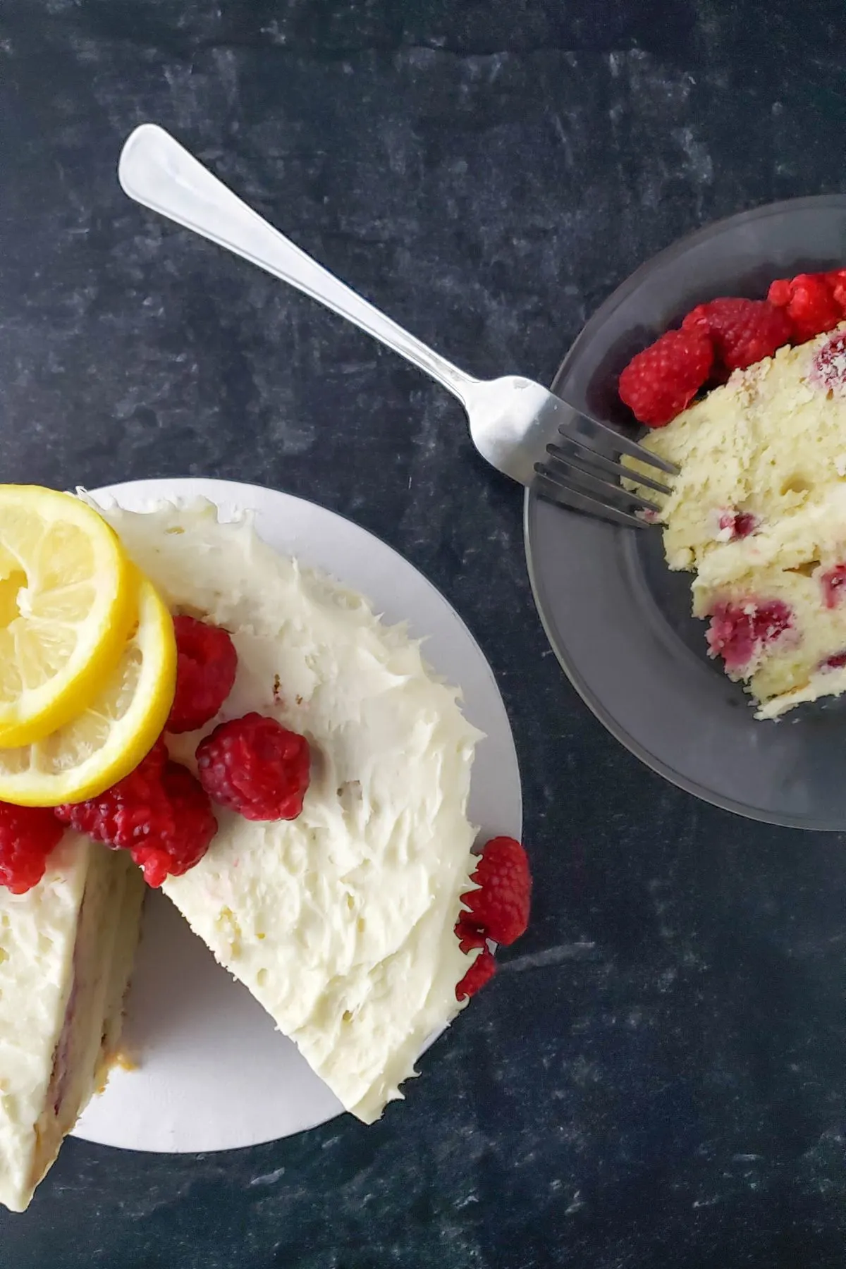 A piece of lemon raspberry cake and the rest of the cake on a separate plate. 