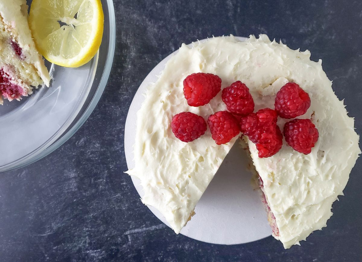 Looking down on a plate with a lemon raspberry cake with a piece missing. 