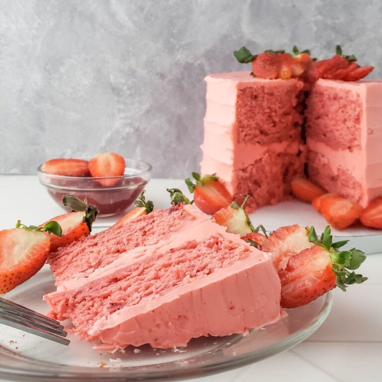 A slice of homemade strawberry gluten free dairy free cake sitting in front of the rest of the cake.