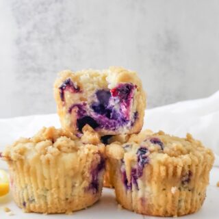 A stack of lemon blueberry muffins with one split open on top fo the pile.