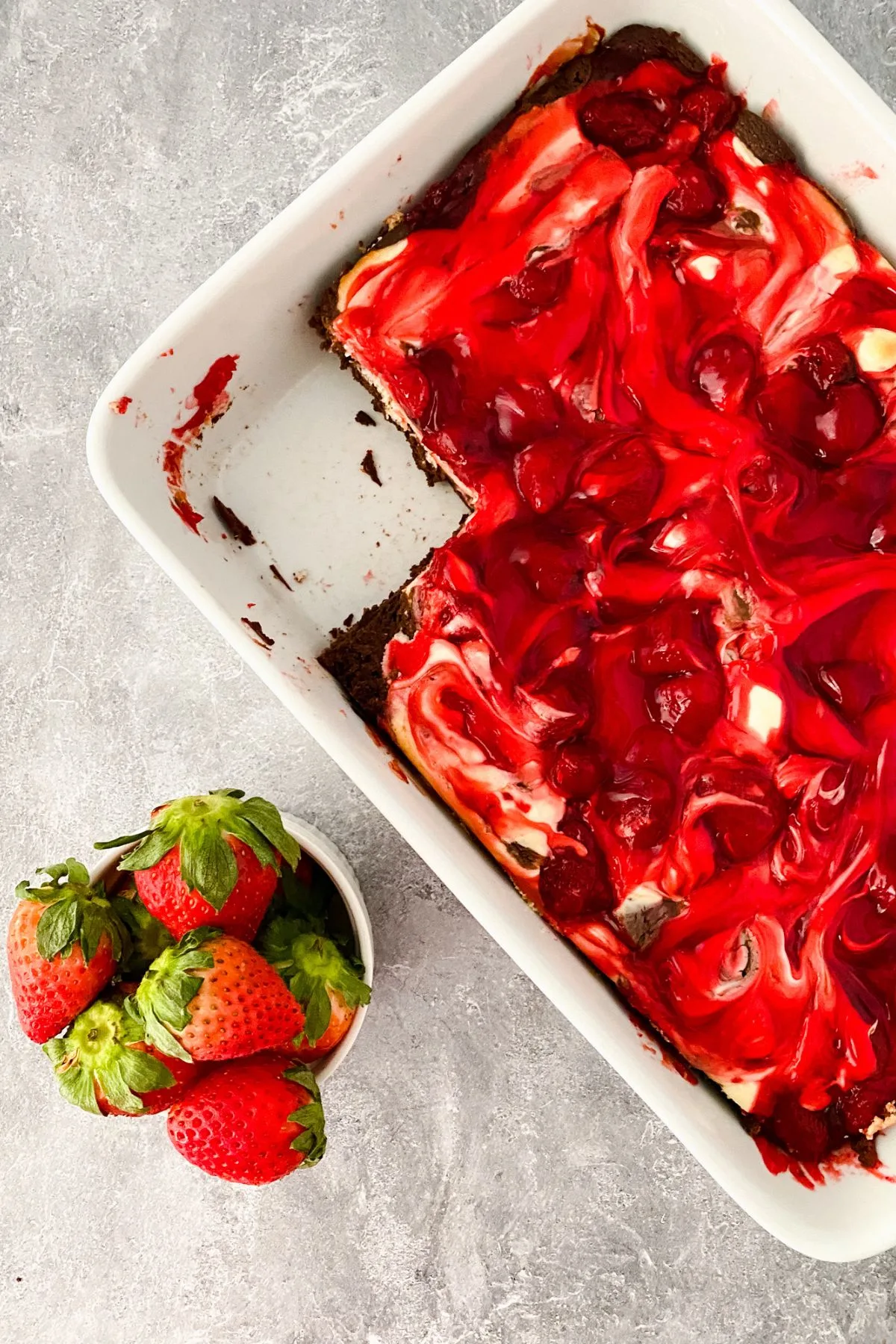 A baking dish of strawberry cheesecake brownies with a piece missing.