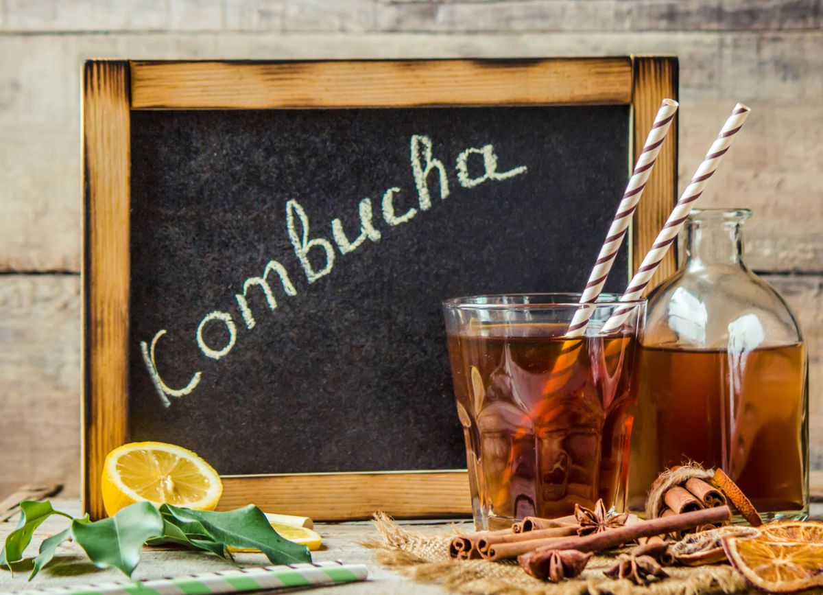 A chalkboard that says kombucha with a glass of it and straws.