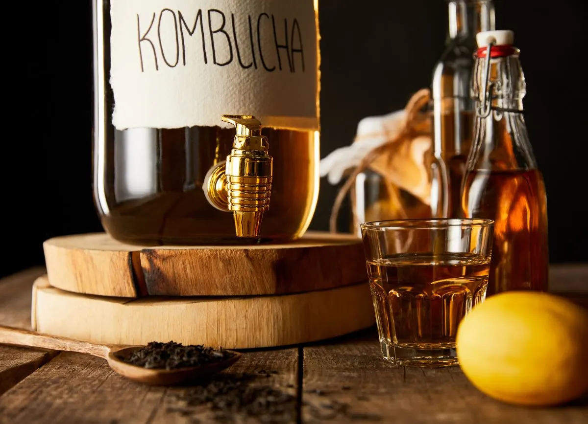 A jar of kombucha and a glass of it on wooden slabs.