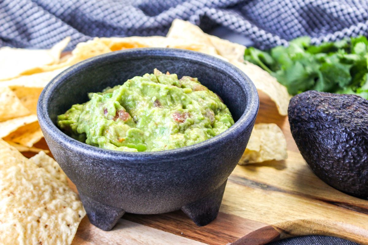 A bowl of guacamole with an avocado next to it.