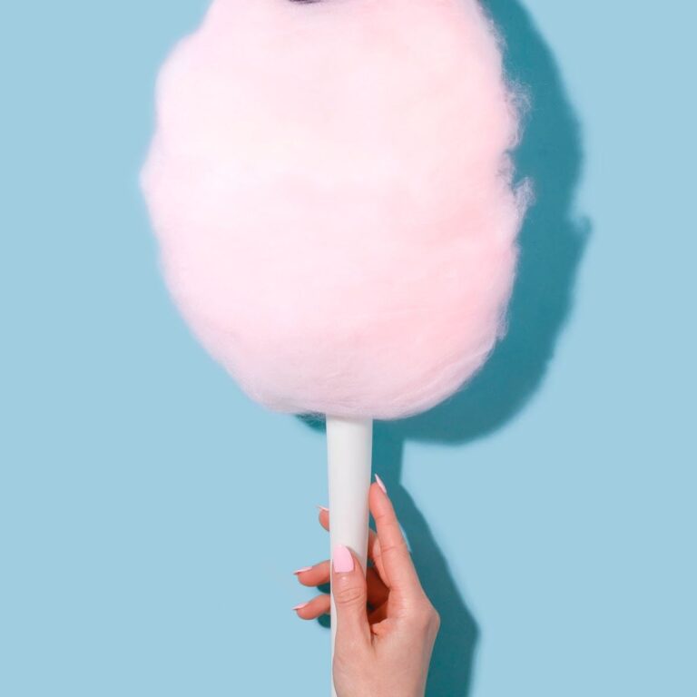 A hand holding some cotton candy on a white holder.
