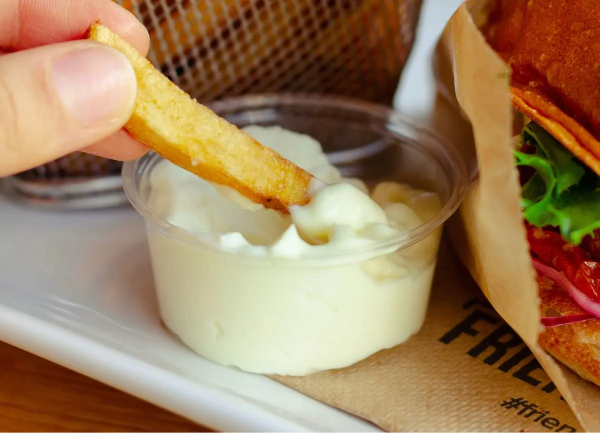Fry being dipped in container of mayo.
