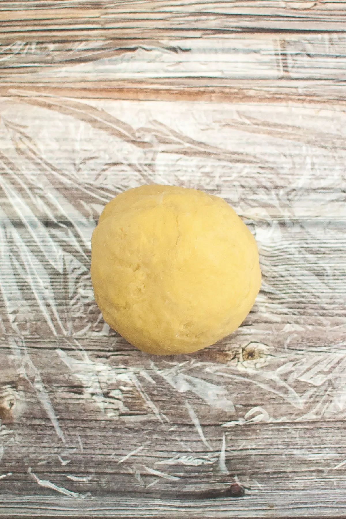 A ball of pasta dough sitting on plastic wrap.