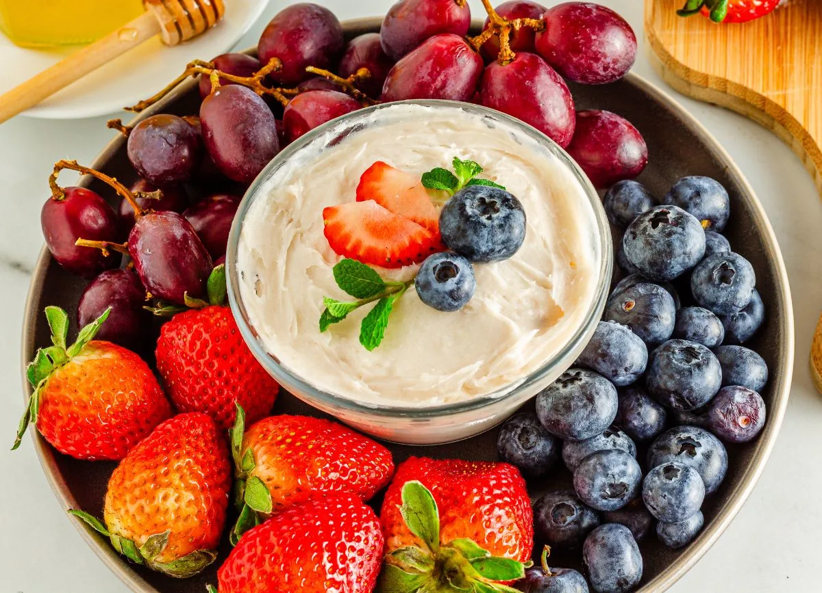 A bowl of fruit dip surrounded with fresh fruit.
