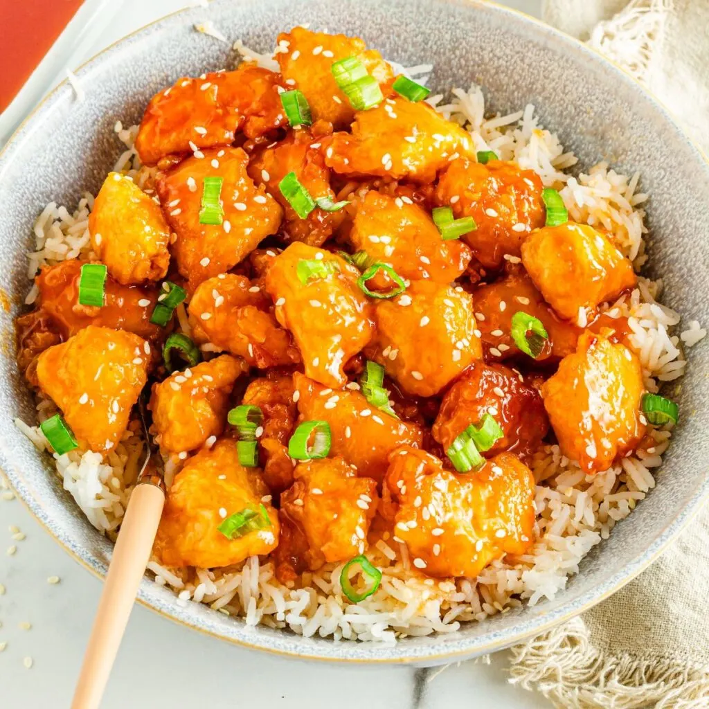 Closely looking at a bowl of Orange Chicken and rice.