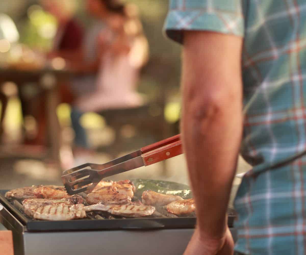 A man standing at the grill grilling chicken.
